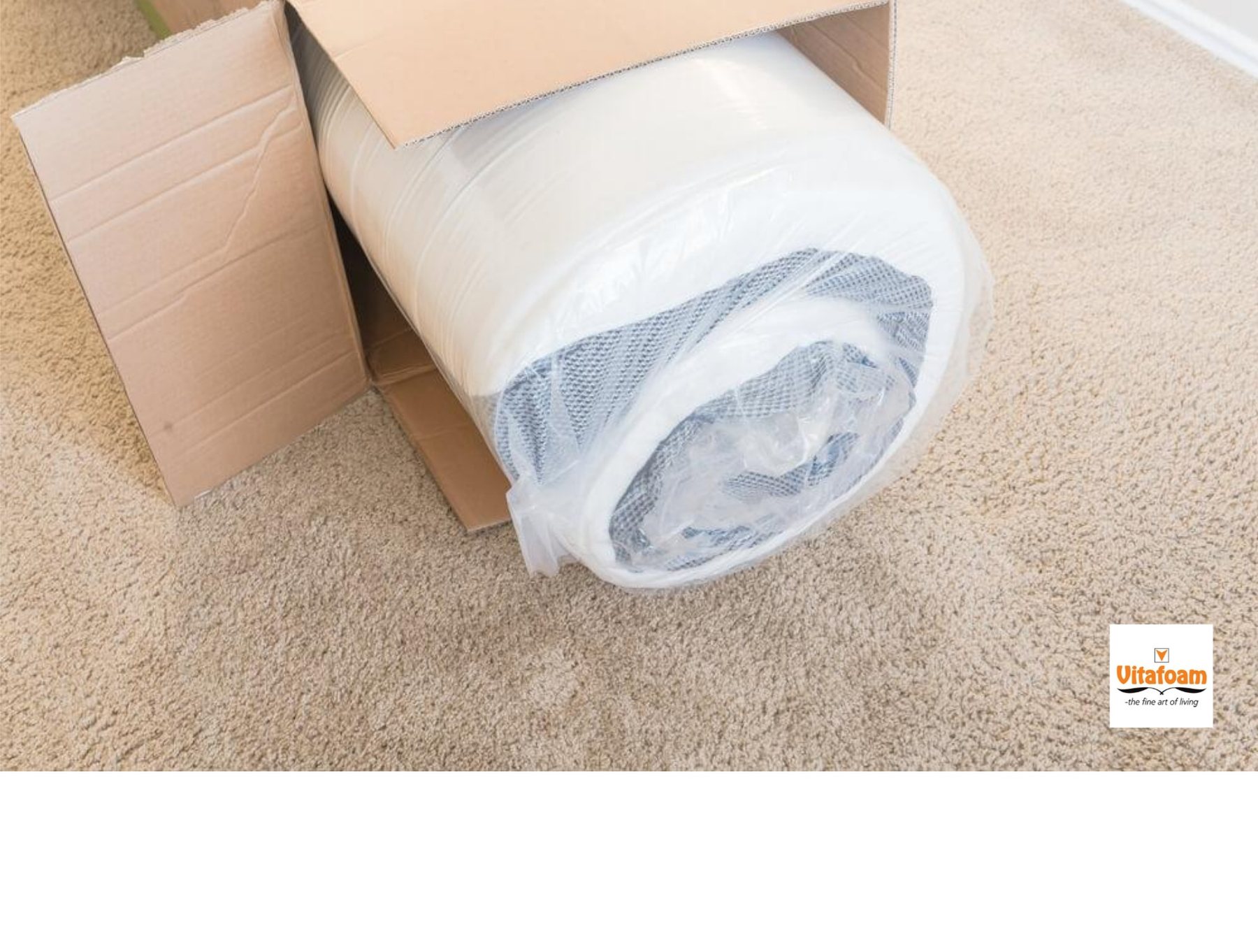 A rolled Vitafoam mattress in its protective wrap emerging from an opened cardboard box